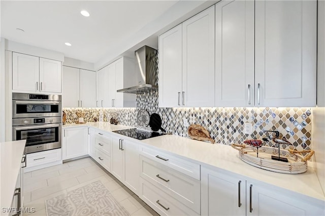 kitchen featuring stainless steel double oven, black electric cooktop, light countertops, backsplash, and wall chimney exhaust hood