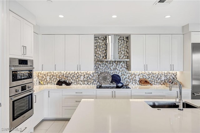 kitchen featuring wall chimney exhaust hood, appliances with stainless steel finishes, a sink, and light countertops