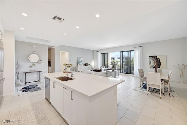 kitchen with light countertops, visible vents, a kitchen island with sink, a sink, and dishwasher