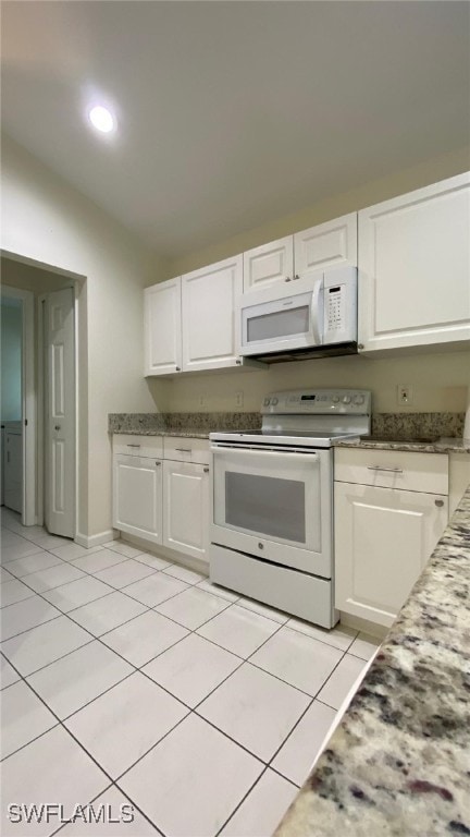 kitchen with light tile patterned floors, white appliances, vaulted ceiling, and white cabinets