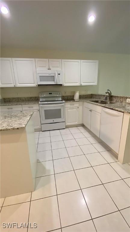 kitchen with white appliances, light tile patterned floors, white cabinets, light stone counters, and a sink