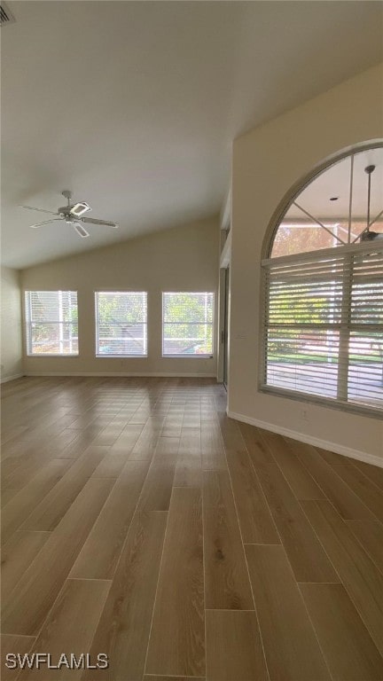 empty room with vaulted ceiling, plenty of natural light, wood finished floors, and baseboards