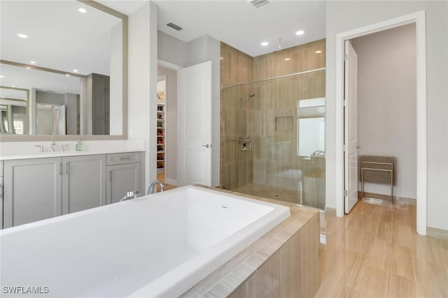 full bath with a walk in closet, tiled bath, visible vents, vanity, and tiled shower