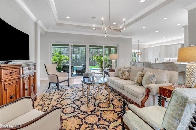 living area featuring a notable chandelier, visible vents, light wood-style floors, ornamental molding, and a tray ceiling