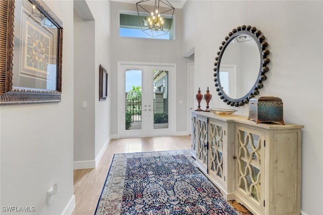 foyer entrance with french doors, a towering ceiling, an inviting chandelier, light wood-type flooring, and baseboards