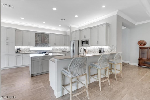 kitchen with a breakfast bar, stainless steel appliances, gray cabinets, wall chimney range hood, and a peninsula