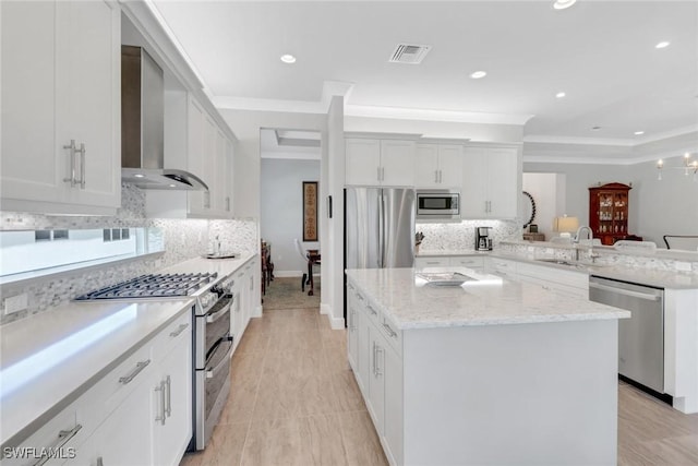 kitchen with stainless steel appliances, a peninsula, a sink, visible vents, and wall chimney range hood