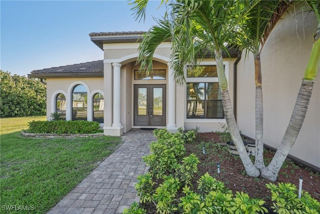 property entrance with a tiled roof, french doors, a yard, and stucco siding