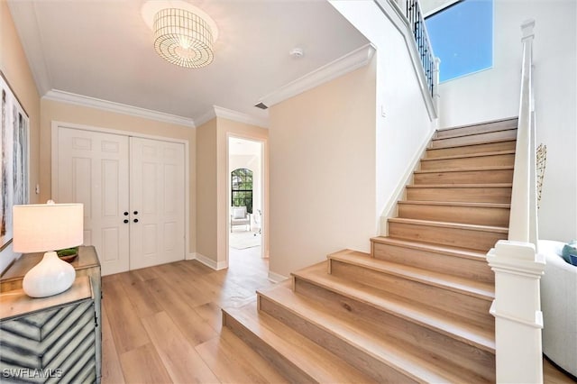 entrance foyer with light wood-style floors, crown molding, stairway, and baseboards