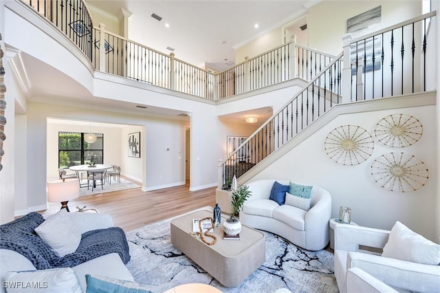 living room featuring a towering ceiling, stairway, ornamental molding, wood finished floors, and baseboards