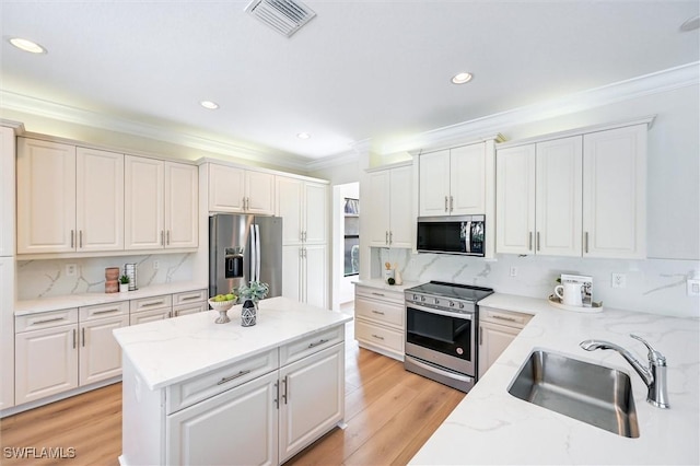 kitchen with stainless steel appliances, a sink, visible vents, ornamental molding, and light wood finished floors