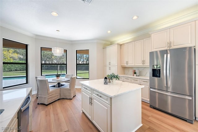 kitchen with appliances with stainless steel finishes, plenty of natural light, ornamental molding, and light wood finished floors