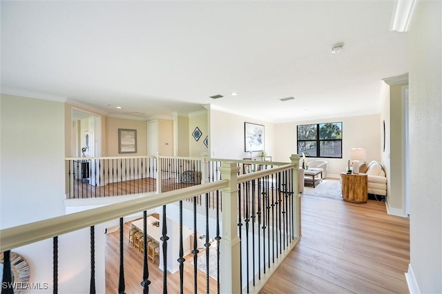 hall with light wood-style floors, visible vents, crown molding, and baseboards