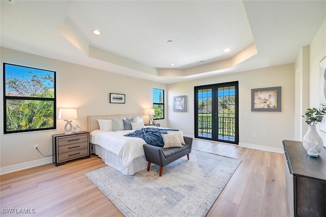 bedroom with access to exterior, a raised ceiling, light wood finished floors, and french doors