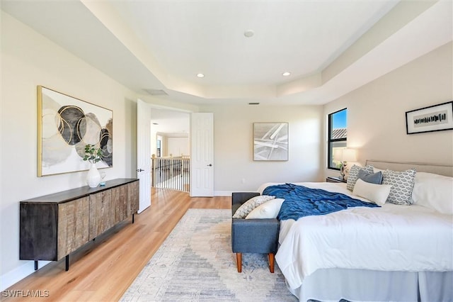 bedroom with light wood-style floors, a tray ceiling, baseboards, and recessed lighting