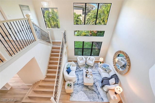 living area featuring stairway, wood finished floors, a towering ceiling, and baseboards