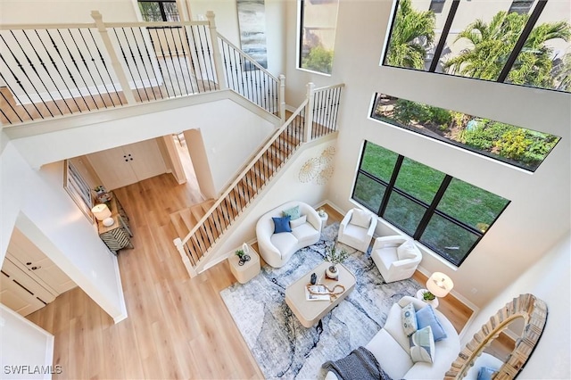 living area with stairs, a wealth of natural light, a towering ceiling, and wood finished floors