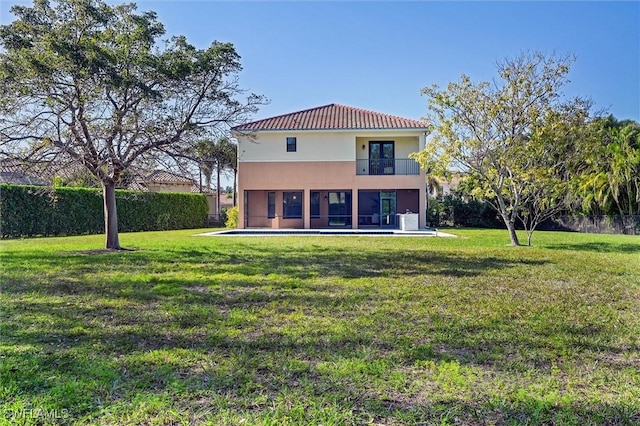 rear view of house with a lawn, fence, a balcony, and stucco siding