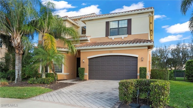 mediterranean / spanish-style home featuring an attached garage, a tiled roof, decorative driveway, and stucco siding