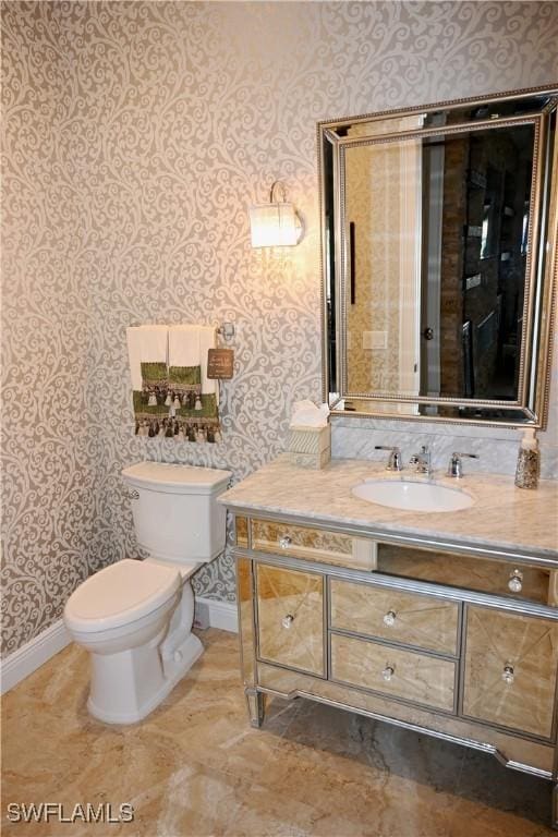 bathroom with baseboards, vanity, toilet, and wallpapered walls