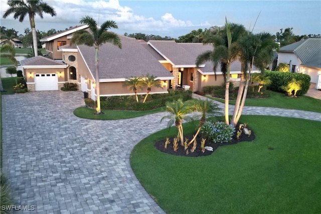 view of front of house featuring an attached garage, stone siding, decorative driveway, stucco siding, and a front lawn