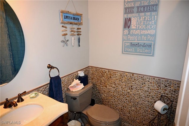 bathroom with tile walls, a wainscoted wall, vanity, and toilet