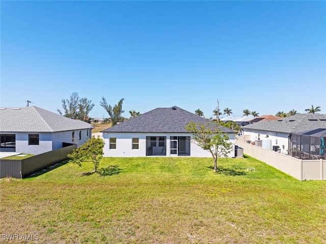 rear view of property featuring a lawn, fence, roof with shingles, and stucco siding