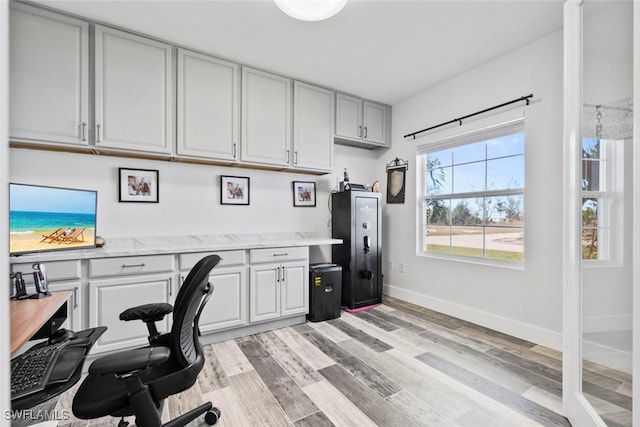 office with baseboards, light wood-style floors, and built in study area