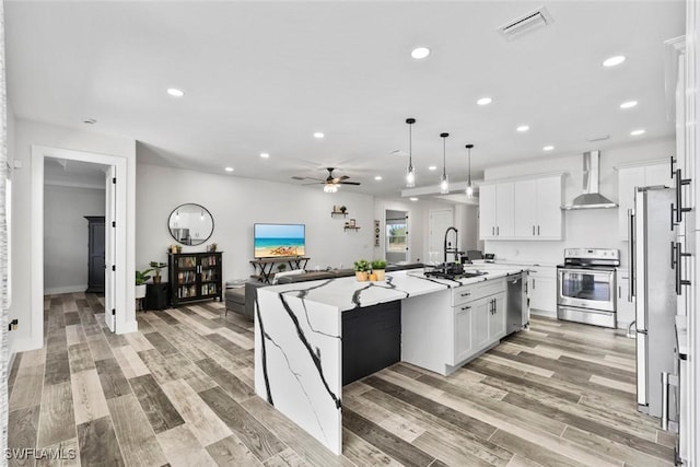 kitchen featuring visible vents, wall chimney range hood, stainless steel appliances, white cabinetry, and a sink