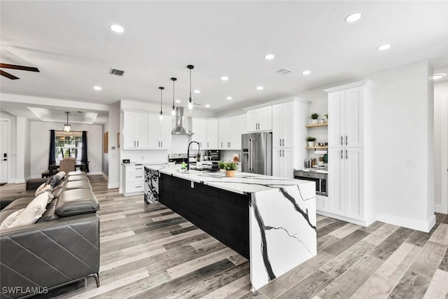 kitchen with open floor plan, white cabinets, appliances with stainless steel finishes, and wall chimney exhaust hood