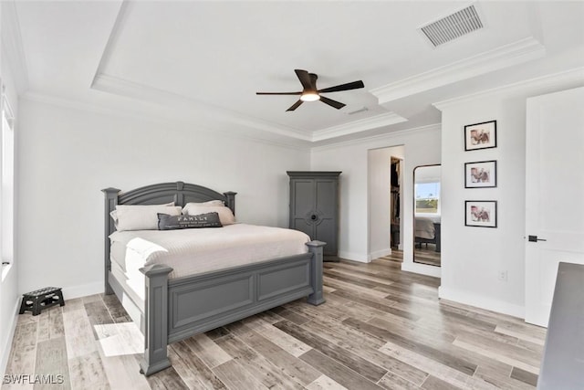 bedroom featuring visible vents, baseboards, crown molding, light wood-style floors, and a raised ceiling