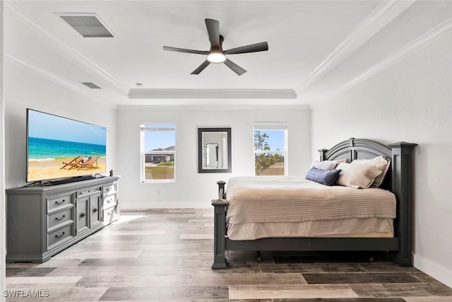 bedroom featuring a tray ceiling, visible vents, multiple windows, and wood finished floors