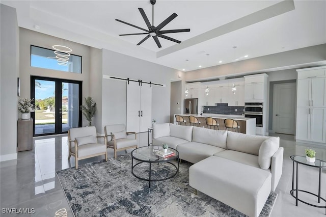 living room with a tray ceiling, a barn door, french doors, a high ceiling, and ceiling fan