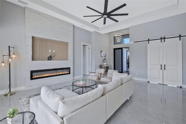 living room featuring ceiling fan, baseboards, a barn door, a towering ceiling, and a glass covered fireplace