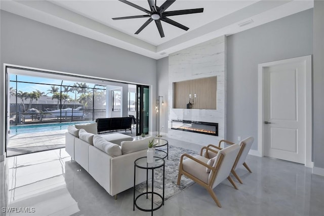 living area featuring a ceiling fan, visible vents, baseboards, a high ceiling, and a fireplace