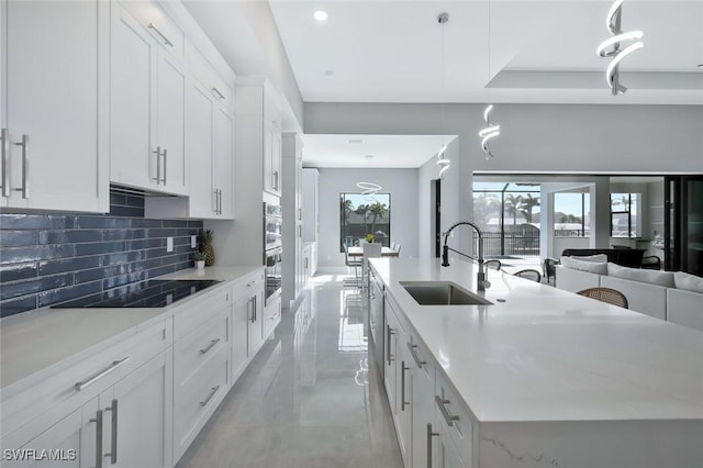 kitchen featuring a sink, backsplash, white cabinetry, black electric cooktop, and a kitchen island with sink