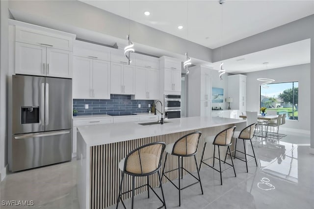 kitchen with a spacious island, a sink, decorative backsplash, appliances with stainless steel finishes, and white cabinetry