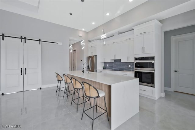 kitchen featuring a kitchen breakfast bar, backsplash, a spacious island, a barn door, and appliances with stainless steel finishes