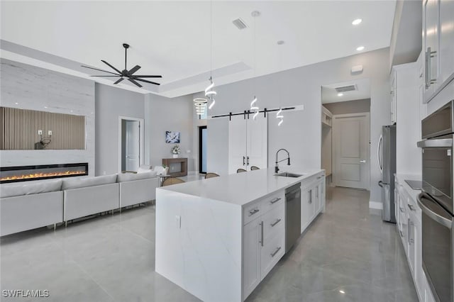 kitchen featuring a sink, white cabinetry, a barn door, stainless steel appliances, and a raised ceiling