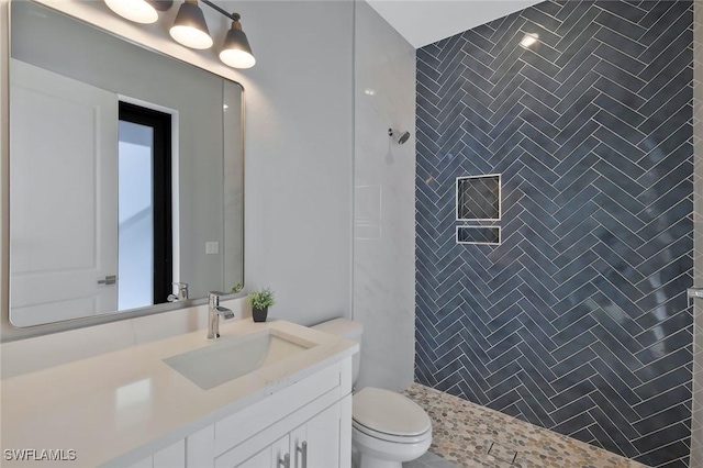 bathroom featuring a tile shower, toilet, and vanity