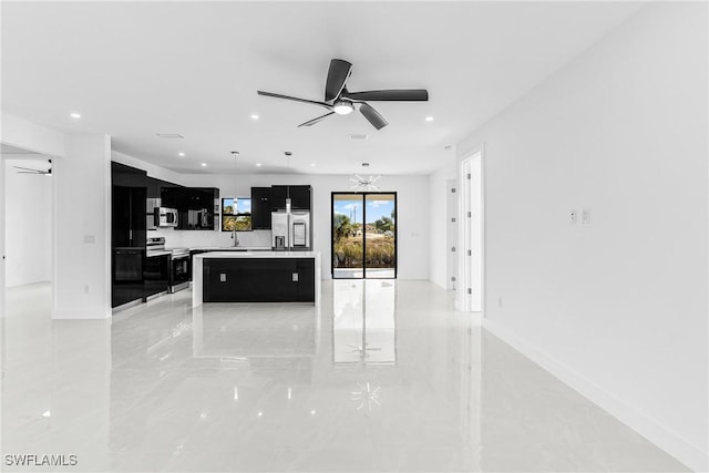 kitchen featuring appliances with stainless steel finishes, dark cabinets, a center island, light countertops, and ceiling fan with notable chandelier