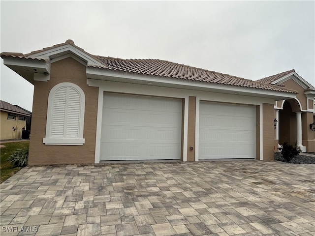 ranch-style house featuring decorative driveway, a tile roof, an attached garage, and stucco siding