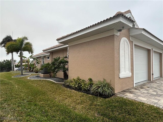 view of home's exterior with a garage, decorative driveway, a yard, and stucco siding