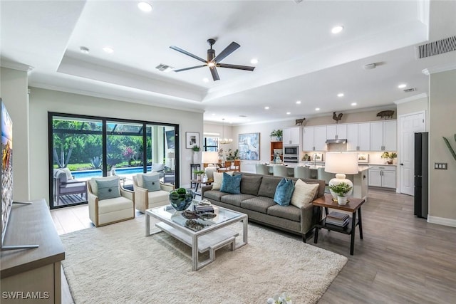 living area featuring visible vents, a raised ceiling, crown molding, and recessed lighting