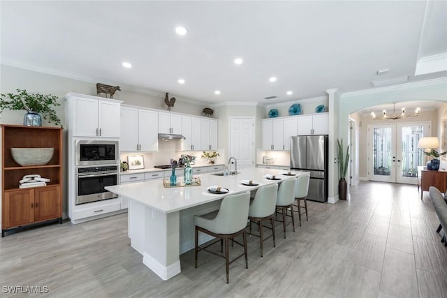 kitchen featuring arched walkways, french doors, stainless steel appliances, a sink, and under cabinet range hood