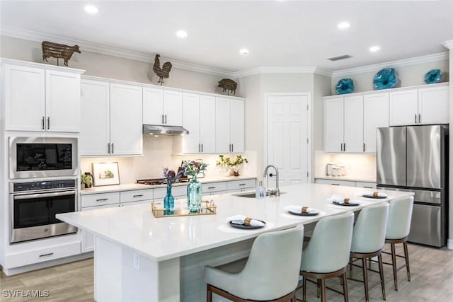 kitchen featuring a kitchen breakfast bar, appliances with stainless steel finishes, a sink, and under cabinet range hood