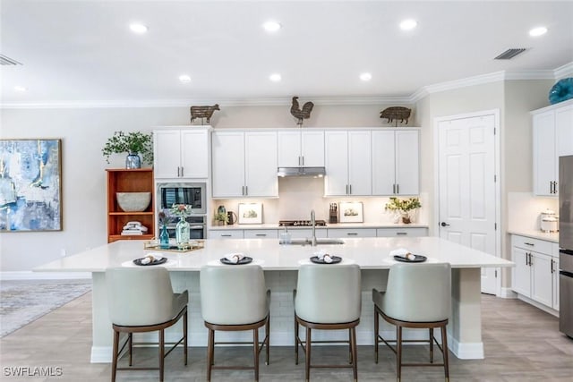 kitchen with a sink, visible vents, light countertops, built in microwave, and a center island with sink