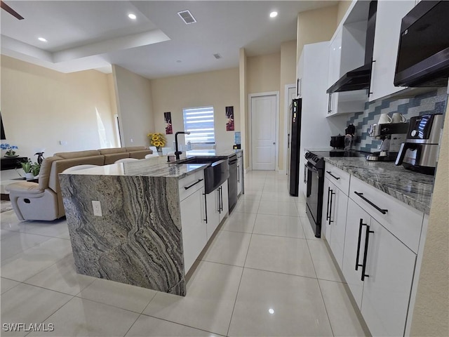 kitchen with light tile patterned floors, electric range, a kitchen island with sink, and a sink