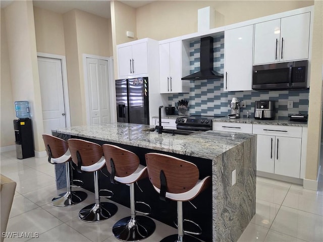 kitchen featuring stainless steel microwave, black fridge with ice dispenser, a kitchen island with sink, light tile patterned flooring, and wall chimney range hood