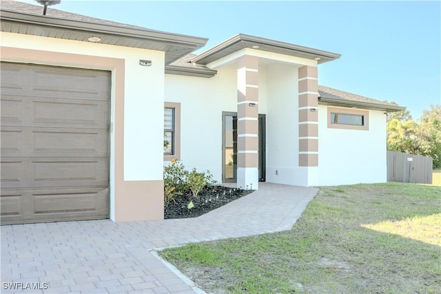 property entrance featuring a lawn, an attached garage, and stucco siding